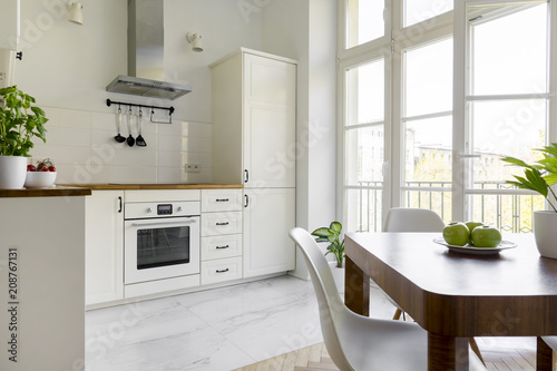 White chair at wooden dining table in simple kitchen interior with window. Real photo