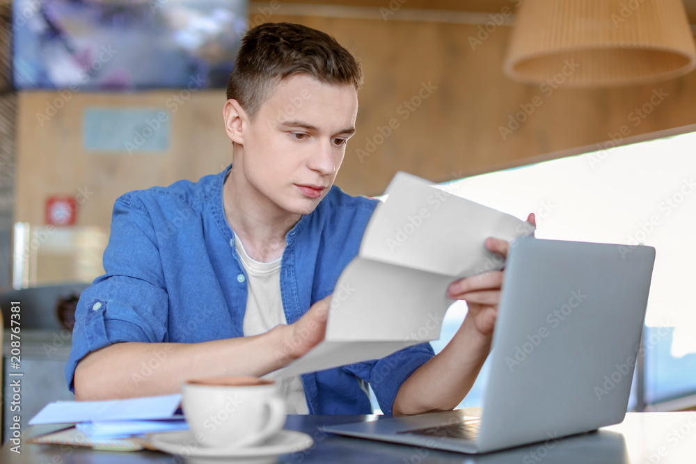 Young man reading letter at table in cafe. Mail delivery