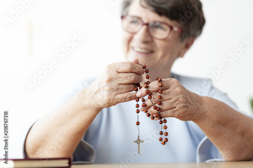 Fototapeta Smiling religious senior woman holding rosary with cross
