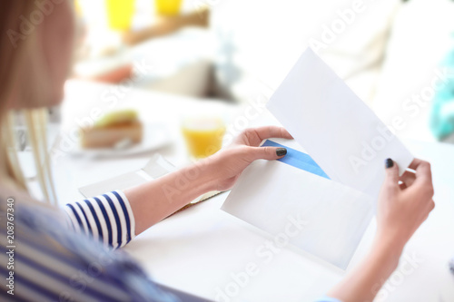 Young woman putting letter into envelope at table in cafe. Mail delivery photo