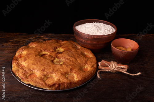 On a dark wooden table american apricot pie, ingredients and tools on black background photo