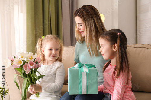 Mother receiving gift and flowers from her cute little daughters at home © Pixel-Shot