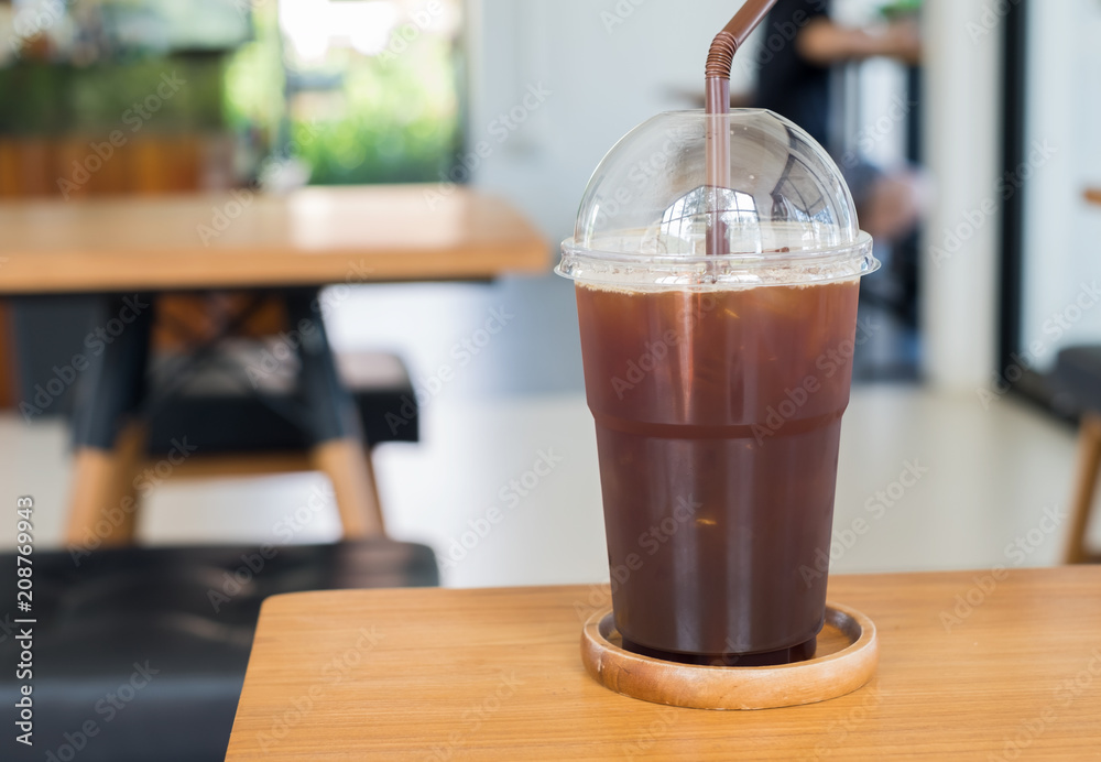 Black iced coffee in clear plastic cup on wood table in the cafe Black iced coffee in clear plastic cup on wood table in the cafe