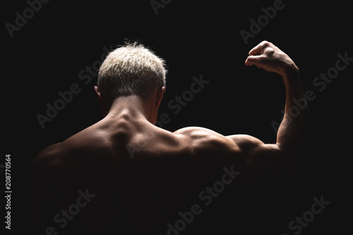 Handsome power athletic man in dramatic light. Strong bodybuilder with perfect shoulders, biceps, triceps, back, delta and chest. Strength and motivation. Bottom view