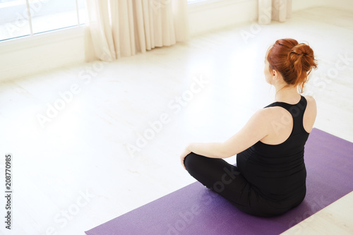Pregnant woman sitting in lotus pose looking in the window