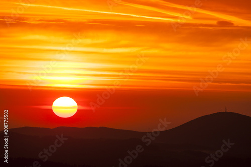 Natural Sunset Sunrise Over highland or mountains. Bright Dramatic Sky And Dark Ground. Countryside Landscape Under Scenic Colorful Sky At Daybreak Dawn. Sun Over Skyline, Horizon. Warm Colors.