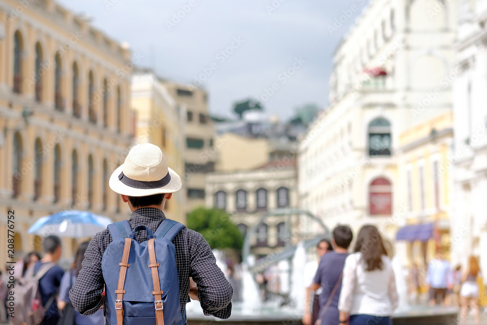 Young man traveling backpacker with hat, Asian hipster traveler standing on Senado Square, landmark and popular for tourist attractions in Macau. Travel concept