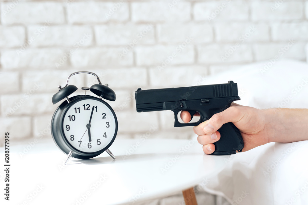 Woken up man is aims gun at alarm clock Stock Photo | Adobe Stock