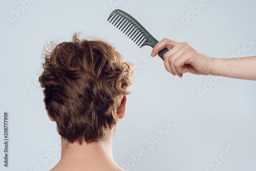 Female hand combs hair of red haired man.