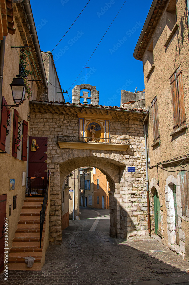 View of stone door, staircase and bell in street at the historical village of Rians, at the sunrise light. Var department, Provence region, southeastern France.