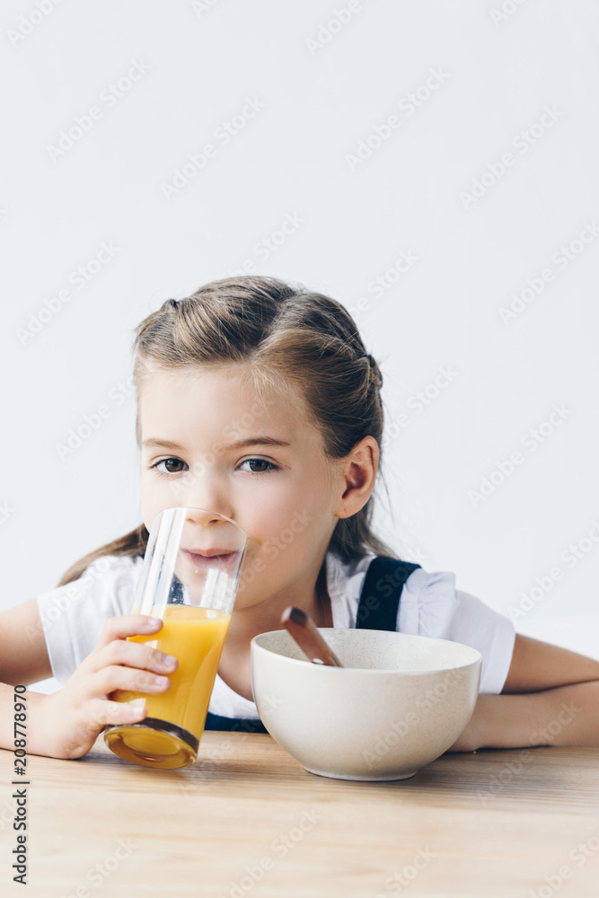 little schoolgirl drinking orange juice during breakfast and looking at camera isolated on white little schoolgirl drinking orange juice during breakfast and looking at camera isolated on white