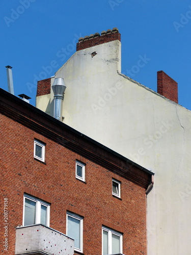 Altes Wohnhaus mit rotbrauner Klinkerfassade vor der Brandmauer des Nachtbarhaus bei blauem Himmel und Sonnenschein in der Marktstraße im Karolinenviertel in der Hansestadt Hamburg photo