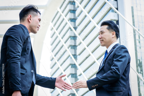 Two asian business have handshake with building and city background.