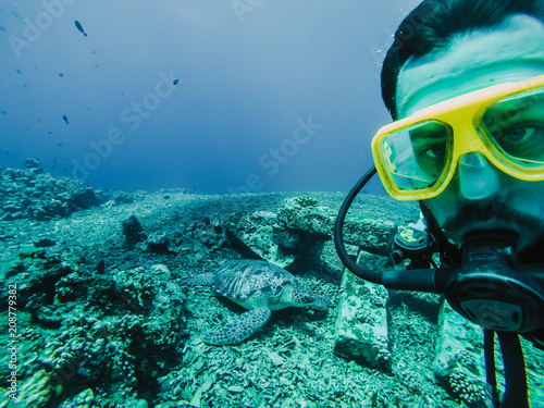 .Young tourist diving in the Gili island, Indonesia, many meters deep, discovering the wild life of the seabed near to a big tourtle. Lifestyle and travel concept.
