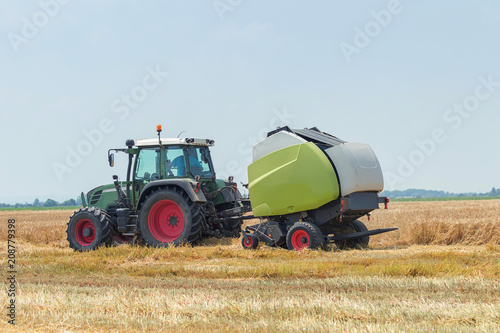 Tractor and round baler discharges. Straw Bales.