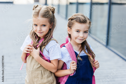 smiling little schoolgirls with pink backpacks on street looking at camera