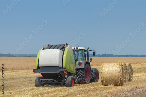 Tractor and round baler discharges. Straw Bales.