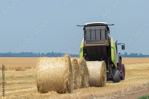 Tractor and round baler discharges. Straw Bales. photo