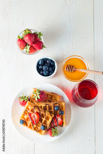 Photo of fresh homemade food made of berry Belgian waffles with honey, chocolate, strawberry, blueberry, maple syrup and cream. Healthy dessert breakfast concept with juice. 