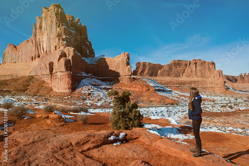 Beautiful woman with backpack hiking along a scenic canyon overlook in Arches National Park in Utah