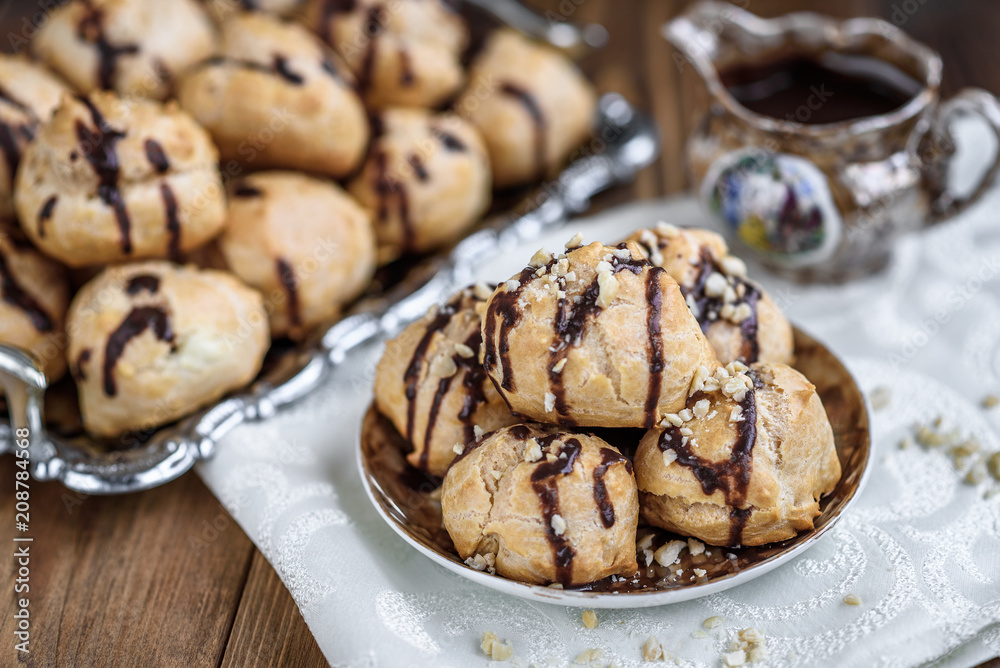 Profiteroles is a delicious culinary dishes of French cuisine with chocolate icing and nuts. Delicious profiteroles dessert on plate on dark wooden background.