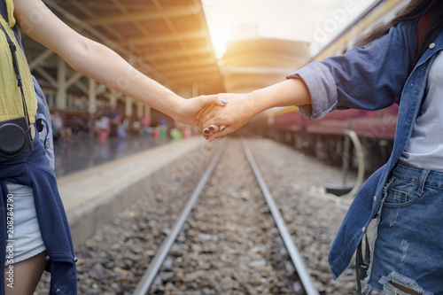 Couple friendship holding hand on path way. Young women reaching hands together on train track. Traveler girl having fun at railway station.