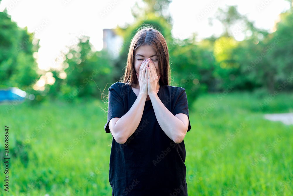 The brunette girl in summer outdoors. In a black T-shirt everyday wear. He covers his mouth with his hands. Happy laughing laughs with her hands over her mouth. Emotions of happiness and pleasure. The brunette girl in summer outdoors. In a black T-shirt everyday wear. He covers his mouth with his hands. Happy laughing laughs with her hands over her mouth. Emotions of happiness and pleasure.
