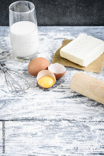 Bakery ingredients - flour, eggs, butter, milk, sugar on grey wooden table. Homemade bakery cooking.