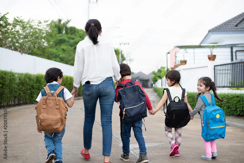 Obraz premium Group of preschool student and teacher holding hands and walking to home. Mom bring her children go to school together. Back to school and Education concept. People and lifestyles theme. Back view