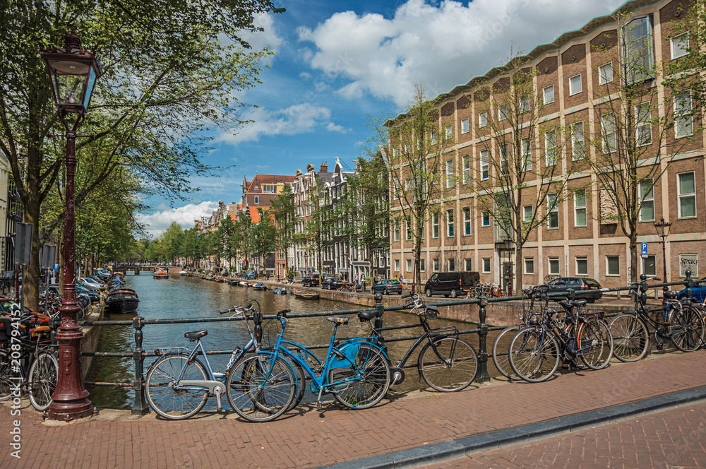 Bridge on canal with iron balustrade, old buildings and bicycles in Amsterdam. Famous for its huge cultural activity and full of graceful canals. Northern Netherlands.