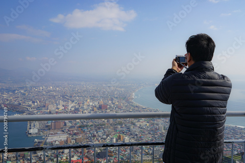 Asian male tourist taking photo of Hakodate town from Mt. Hakodate view point.