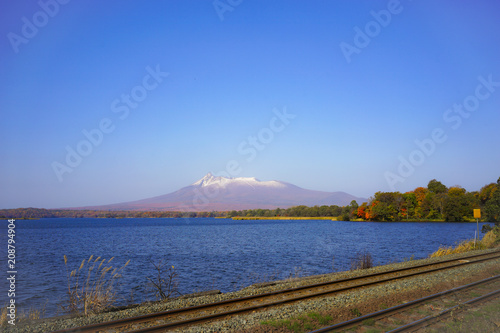 Beautiful view of Mt. Komagatake alongside railway track, near Onuma park, Hakodate, Hokkaido, Japan. During autumn season with clear blue sky.