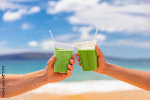 Couple toasting healthy juice drinks together at beach restaurant. Detox smoothie drink toast at summer vacations holidays. Fruit juicing weight loss diet.