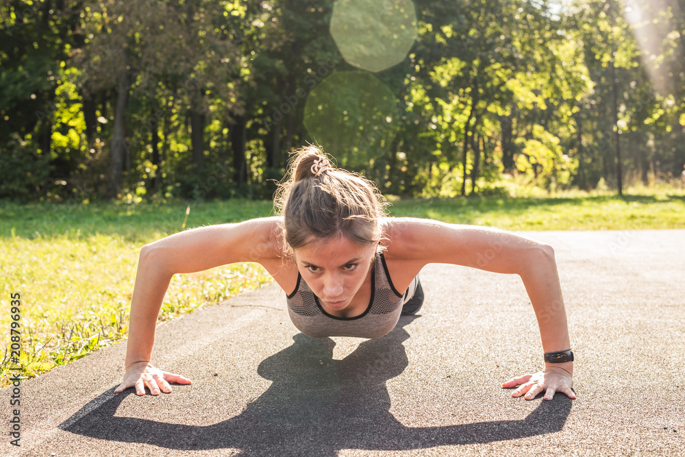 Fototapeta premium Fitness woman doing push-ups during outdoor cross training workout. Beautiful young and fit fitness sport model training outside in park