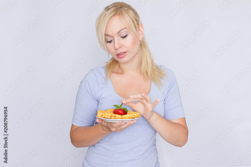 A happy blonde is holding a plate with Belgian waffles in her hands. Breakfast is decorated with strawberries and mint leaves. Concept: home food.