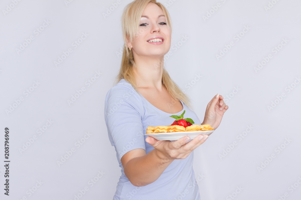 A happy blonde is holding a plate with Belgian waffles in her hands. Breakfast is decorated with strawberries and mint leaves. Concept: home food. A happy blonde is holding a plate with Belgian waffles in her hands. Breakfast is decorated with strawberries and mint leaves. Concept: home food.