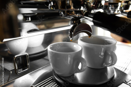 Italian espresso machine on a counter in a restaurant dispensing freshly brewed coffee into two small cups