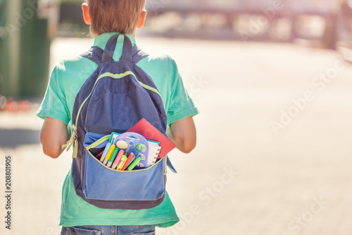 Schoolboy with full backpack go to school. Back view