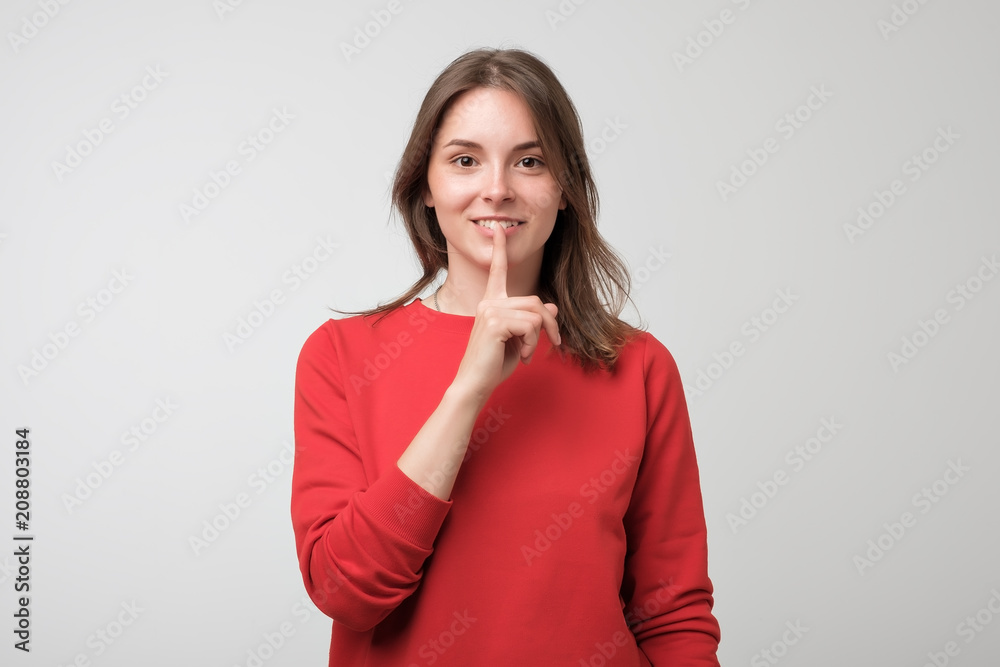 Beautiful european woman in red pulover showing silence sign on white background Beautiful european woman in red pulover showing silence sign on white background
