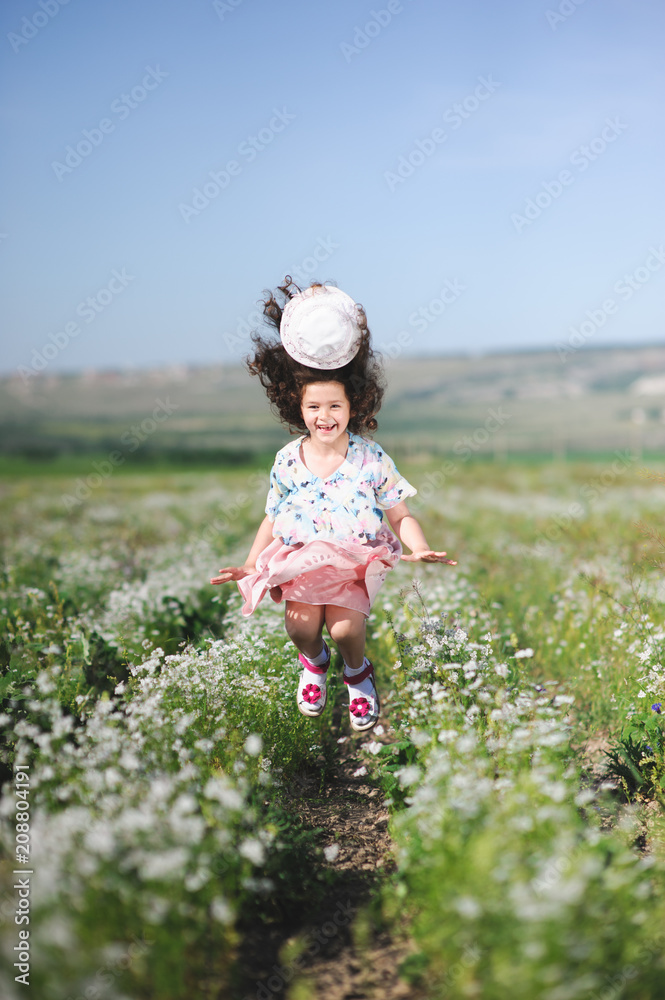 pretty happy little girl jumping with hat flying off her head in flower field pretty happy little girl jumping with hat flying off her head in flower field