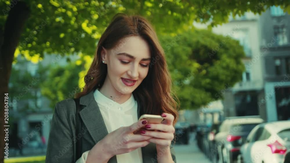 Close up view of young attractive caucasian woman in a formal outfit using her smartphone outside the office, in the park. Modern communication, texting, being online. Female portrait Close up view of young attractive caucasian woman in a formal outfit using her smartphone outside the office, in the park. Modern communication, texting, being online. Female portrait