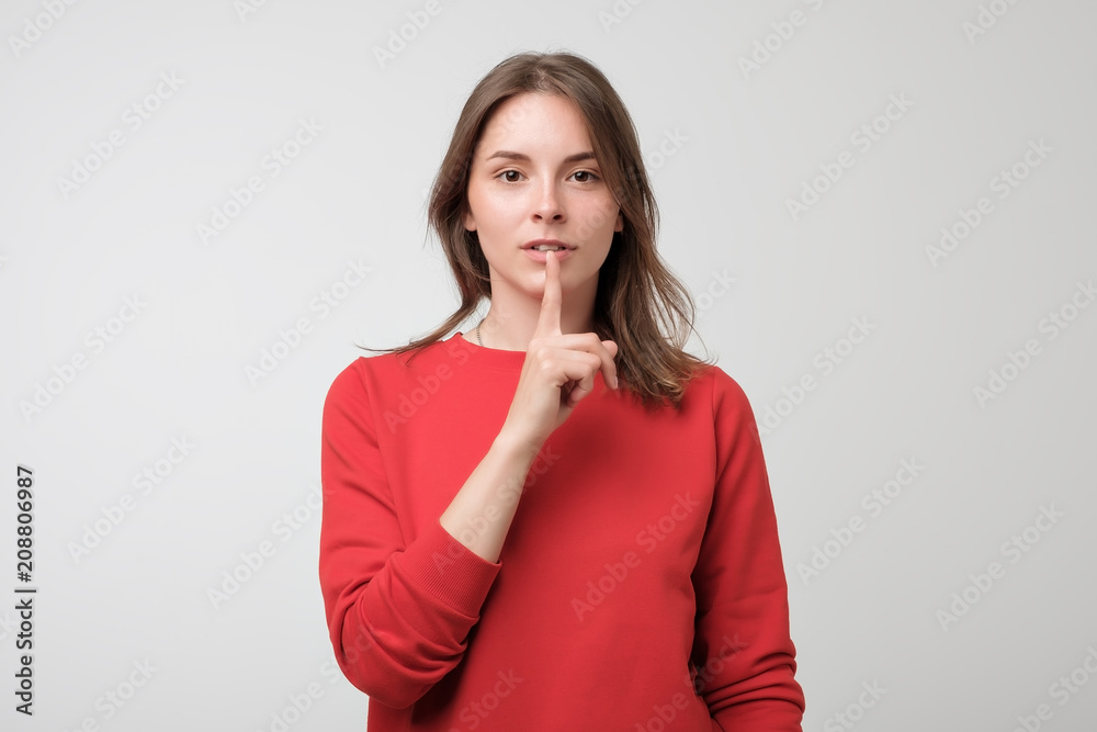 Beautiful european woman in red pulover showing silence sign on white background Beautiful european woman in red pulover showing silence sign on white background