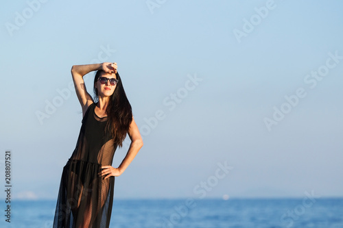 attractive young woman with long dark hair in black swimwear and transparent dress. concept of happy holiday and resort time