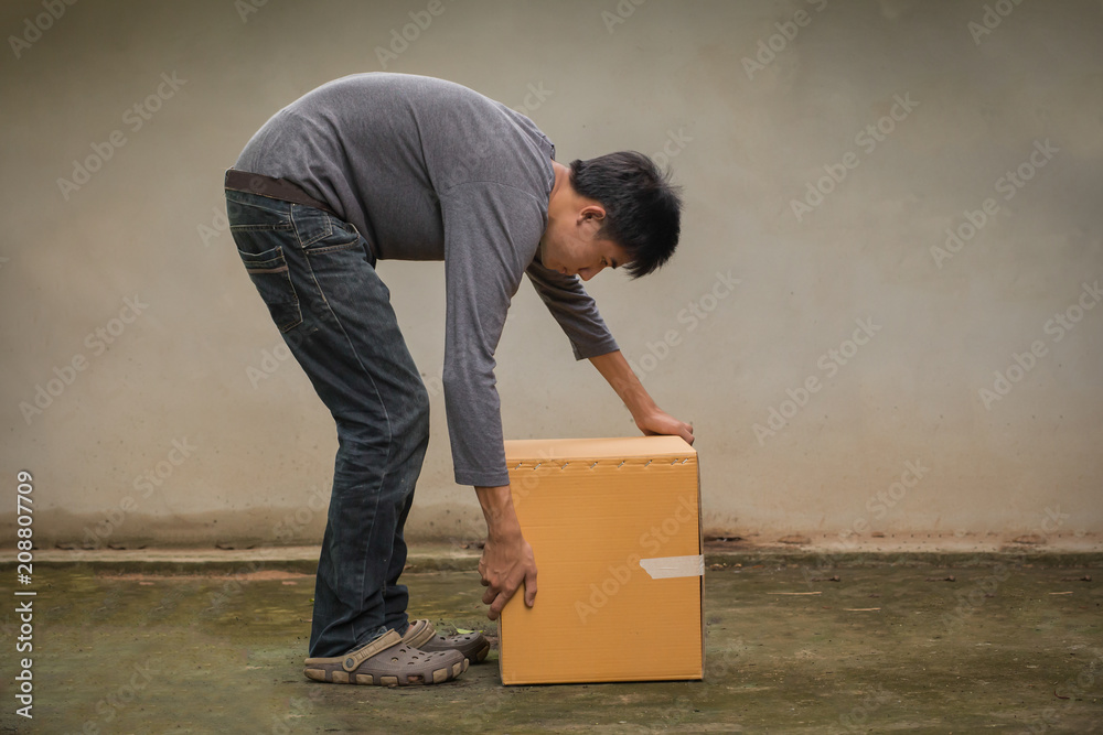  young man bent down, raised cardboard box in an ergonomic posture. - obrazy, fototapety, plakaty 