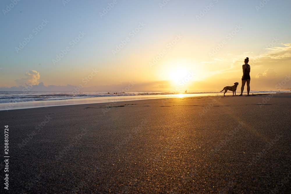 Silhoette of woman playing with dog on sand beach.