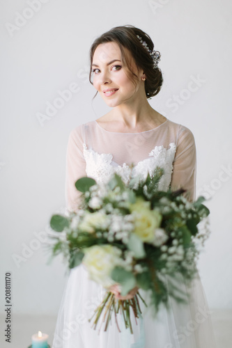 Beautiful bride in front of wedding decorations with flowers and candles. Bouquet in the hands and details. The girl is happy, smiling and dancing. Dream wedding dress in modern style