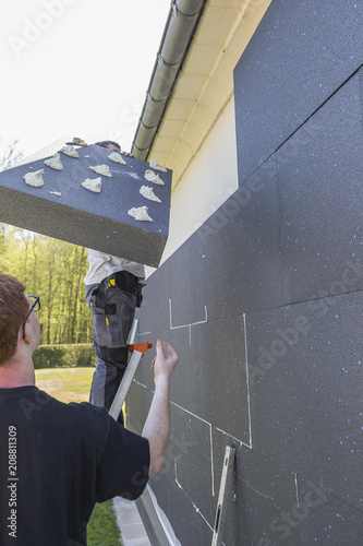 Professional preparing and installing thermal insulating polyurethane sheets for outdoor insulation of a house photo