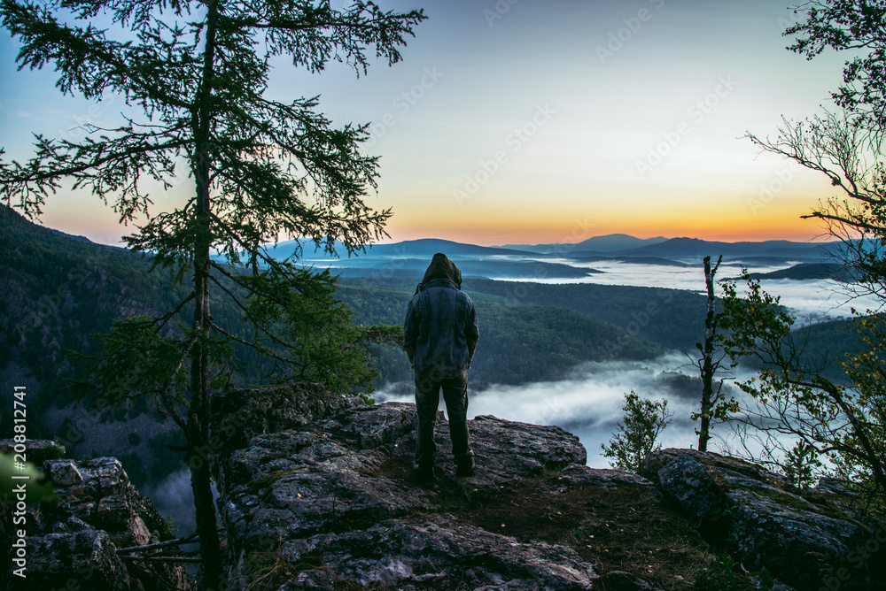 Man hiker standing back on peak of mountains and enjoy to see beautiful landscape view of rocks and mist coming up at summer morning. Man hiker standing back on peak of mountains and enjoy to see beautiful landscape view of rocks and mist coming up at summer morning.