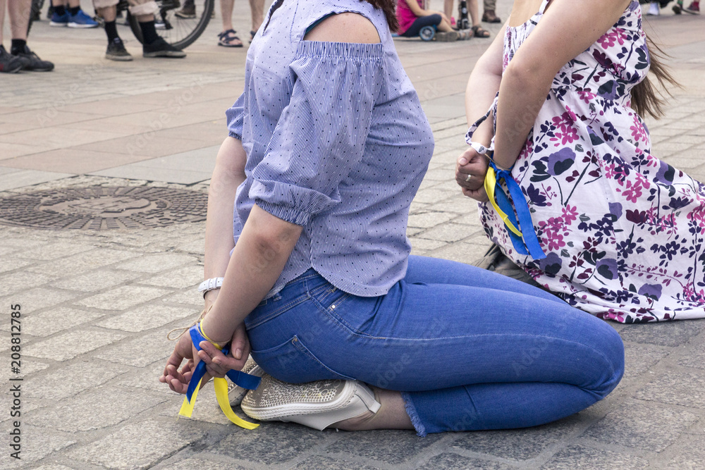 Two women with their hands tied behind their backs sit on their knees