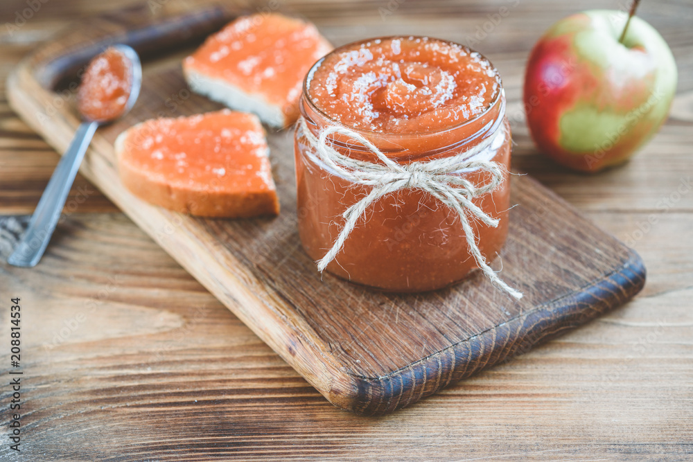 Apple jam in bank with apples, slice of bread with jam and spoon of jam on linen fabric on wooden background. Apple jam in bank with apples, slice of bread with jam and spoon of jam on linen fabric on wooden background.